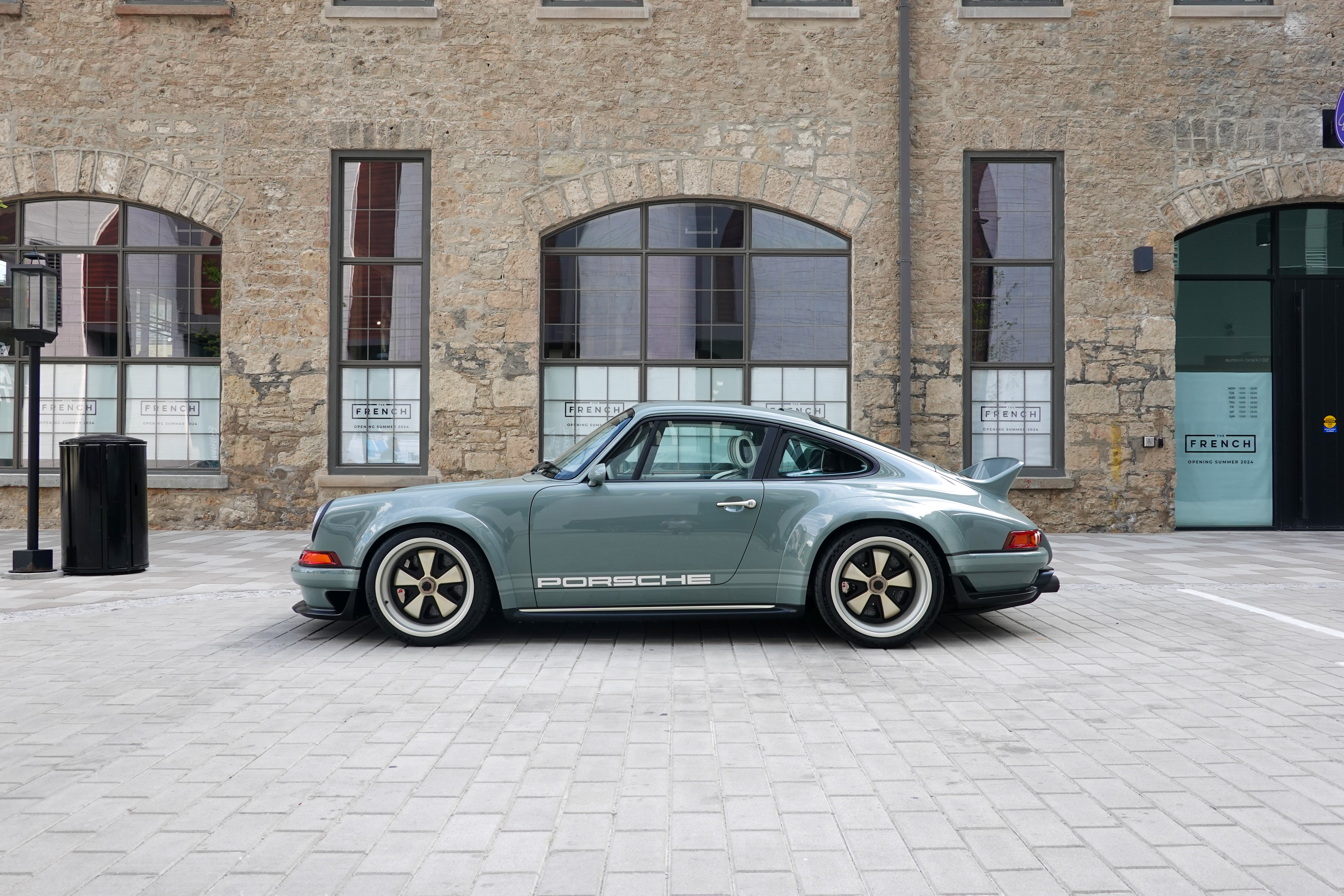 A silver Porsche parked against a historic stone building