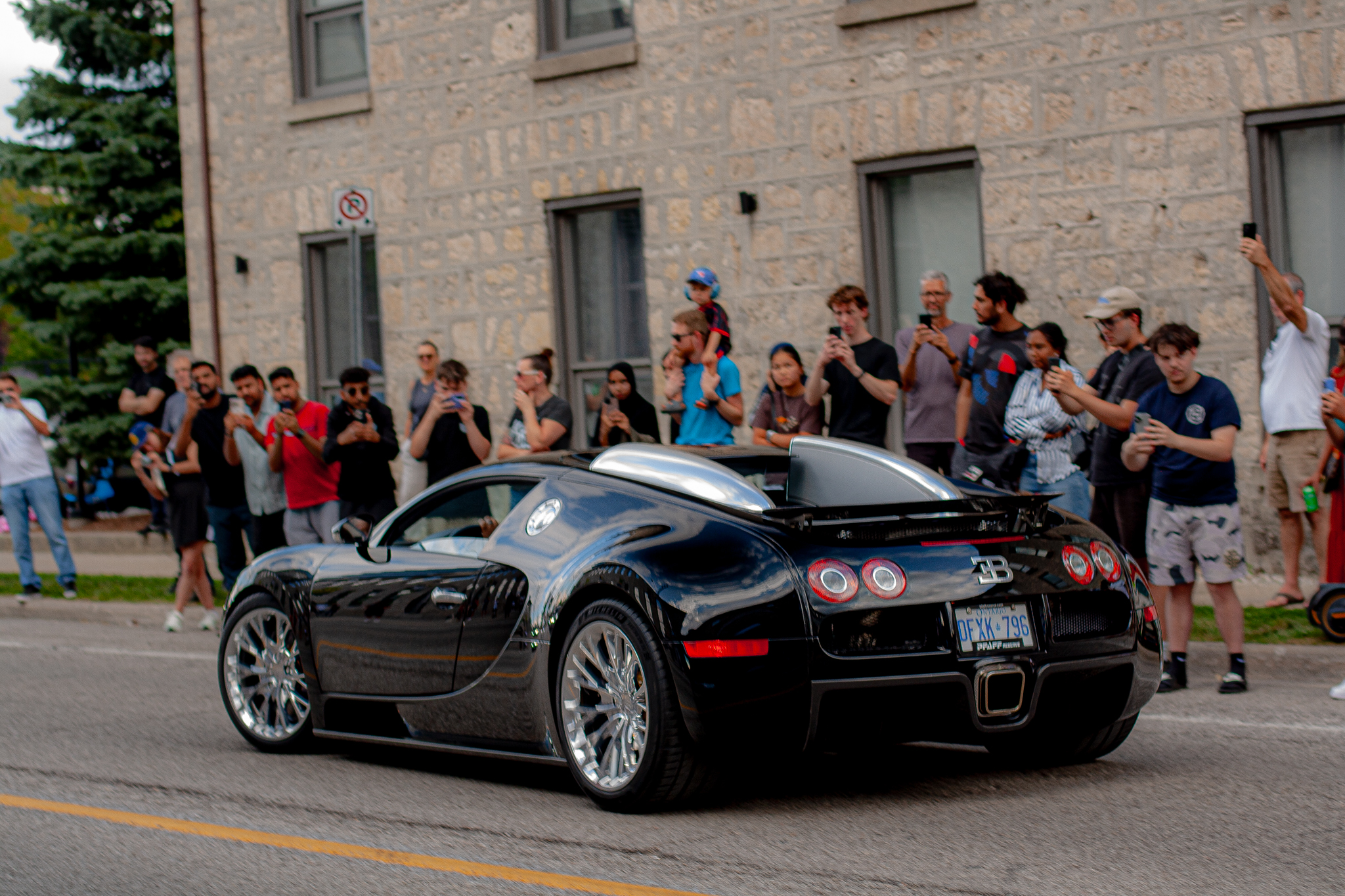 A black Bugatti passing a crowd at the charity car show